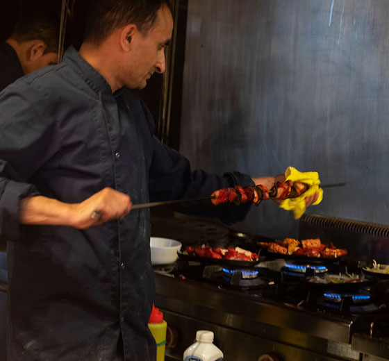 Een close-up van de handen van een chef-kok die een kipgerecht bereidt in het Indian Naan Restaurant