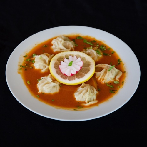 Bowl of momo soup with lemon slice and cilantro